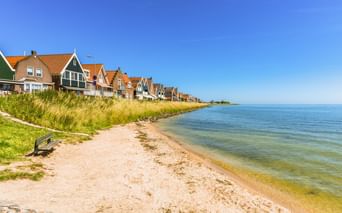 Sandstrand in Volendam mit traditionellen niederländischen Häusern mit orangen Ziegeldächern entlang der Küste. Klarer blauer Himmel.