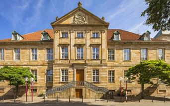 Barockes Sandsteingebäude mit verziertem Giebel und doppelter Freitreppe in Osnabrück. Die Bischöfliche Kanzlei hat ein rotes Ziegeldach.