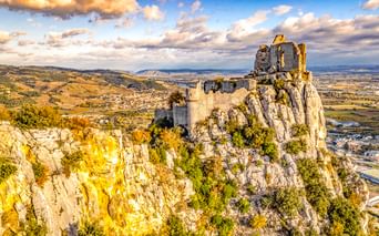 Mittelalterliche Ruine des Château de Crussol auf einem Felsen bei Valence, Frankreich. Steinmauern krönen den Gipfel mit Talblick unter blauem Himmel.