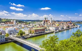 Panoramablick auf Passaus historische Altstadt an der Donau mit bunten Gebäuden, Kirchtürmen und einer Brücke unter blauem Himmel.