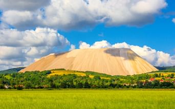 Großer weißer Salzberg Monte Kali erhebt sich über grüne Felder und Dorfhäuser in Heringen an der Werra unter blauem Himmel mit weißen Wolken.