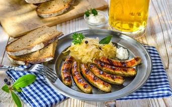 Teller mit gegrillten Würstchen, Sauerkraut und Brotscheiben auf einem Holztisch, begleitet von einem Glas Bier in Franken.