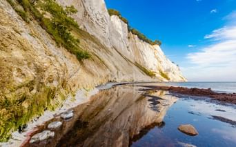 Dramatische weiße Kreidefelsen von Møns Klint auf der Insel Møn, die vom Strand aufragen, mit grüner Vegetation oben und ruhigem blauen Meer.