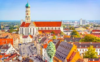 Luftaufnahme der Basilika St. Ulrich und Afra mit markanter grüner Zwiebelkuppel und rotem Dach, die Augsburgs historische Altstadt überragt.