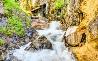 Rauschender Wasserfall in enger Felsschlucht mit moosbewachsenen Wänden und Holzstegen im Zammer Lochputz in Österreich.