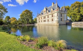Château d'Azay-le-Rideau, ein weißes Renaissance-Schloss mit Türmchen und Schieferdach, spiegelt sich im umgebenden Wassergraben unter blauem Himmel.