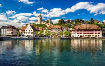 Blick auf Schaffhausen am Rhein mit historischen Gebäuden und der Festung Munot auf dem Hügel. Traditionelle Schweizer Architektur spiegelt sich im Rhein.