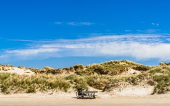 Fahrrad auf einem breiten Sandstrand mit grasbewachsenen Dünen unter blauem Himmel mit weißen Wolken in Belgien.