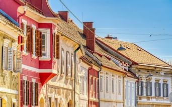 Row of historic buildings with colorful facades in pink, yellow, and white in Bad Radkersburg under blue sky with traditional tiled roofs.