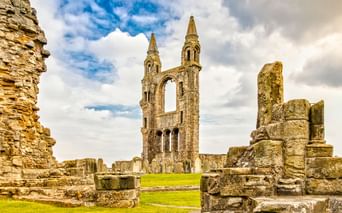 Steinruinen der St Andrews Kathedrale mit hohem gotischem Turm mit zwei Türmen und Bogenfenstern, umgeben von bröckelnden Mauern und grünem Gras.