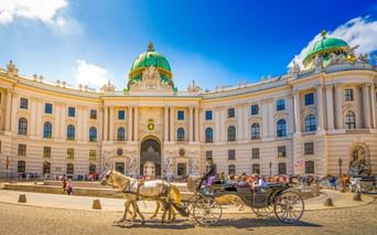 Traditioneller Fiaker im Innenhof der Wiener Hofburg mit ihrer markanten grünen Kuppel und cremefarbenen Barockfassade.