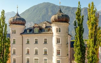 Weißes Rathaus Lienz mit zwei markanten zwiebelförmigen Kupferkuppeln und hohen grünen Pappeln vor Bergkulisse.
