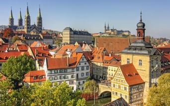 Panoramablick auf Bambergs Altstadt mit roten Ziegeldächern, historischen Fachwerkhäusern, Kirchtürmen und dem Alten Rathaus am Fluss.
