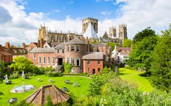 York Minster Kathedrale mit ihren gotischen Türmen erhebt sich über historischen Backsteingebäuden und gepflegten Gärten mit grünen Rasenflächen.