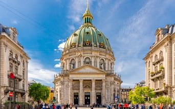 Frederikskirche in Kopenhagen mit markanter grüner Kupferkuppel und goldener Spitze. Die barocke Marmorkirche ist von historischen Gebäuden und Besuchern umgeben.