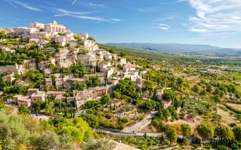 Mittelalterliches Dorf Gordes auf einem felsigen Hang in der Provence, Frankreich. Steingebäude erstrecken sich den Hang hinunter mit Kirche.