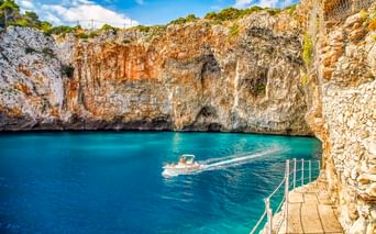 Türkisfarbenes Wasser an der Grotta Zinzulusa in Castro mit Kalksteinklippen, einem Boot in der Bucht und Steinstufen mit Metallgeländer.