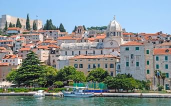 Blick auf die Altstadt von Šibenik vom Wasser aus mit der Jakobskathedrale und ihrer markanten Kuppel, umgeben von historischen Gebäuden.