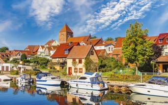 Hafen mit weißen Booten in Plau am See. Historische Stadt mit roten Ziegeldächern und Kirchturm unter blauem Himmel mit weißen Wolken.