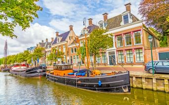 Traditionelle niederländische Boote am Kanal in Harlingen, gesäumt von bunten historischen Gebäuden mit Schornsteinen unter blauem Himmel.