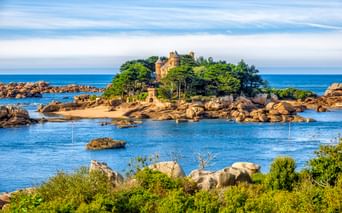 Schloss Costaérès auf einer kleinen Felseninsel, umgeben von blauem Wasser und Granitfelsen. Dichte grüne Vegetation bedeckt die Insel.