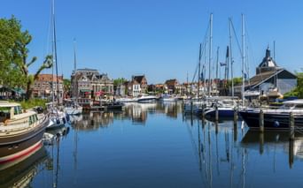 Hafen in Enkhuizen mit Segelbooten am ruhigen Wasser. Historische Gebäude und ein Kirchturm säumen die Uferpromenade unter blauem Himmel.