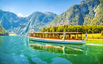 Traditionelles Passagierboot mit Holzkabine auf dem klaren grünen Wasser des Königssees, umgeben von steilen bewaldeten Bergen in Bayern.