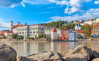 Colorful historic buildings of Passau Old Town along the Danube River, featuring a white tower with red roof and church spires under blue sky.