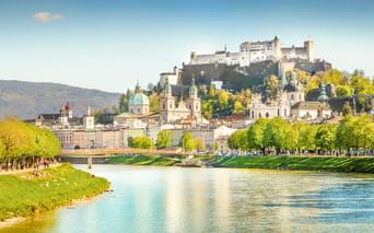 Salzburger Altstadt mit Festung Hohensalzburg auf dem Hügel, barocken Kirchenkuppeln und der Salzach mit grünen Ufern im Frühling.