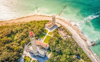 Luftaufnahme des Leuchtturmkomplexes Phare des Baleines auf der Île de Ré mit zwei Leuchttürmen und Gebäuden an einer Küstenspitze mit türkisfarbenem Wasser.