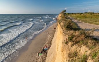 Sandige Steilküste mit Gras oben mit Blick auf die Ostsee bei Prerow. Radfahrer ruhen am Strand unten, während Wellen ans Ufer rollen.