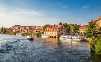 Malerischer Blick auf Bambergs historisches Flussufer mit traditionellen Fachwerkhäusern, Ausflugsbooten und dem Alten Rathaus am Wasser.