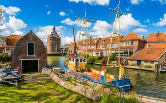 Historischer Hafen von Enkhuizen mit bunten Booten, traditionellen niederländischen Häusern mit orangen Dächern und dem Drommedaris-Turm.