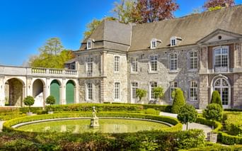 Steinschloss mit formalen Wassergärten in Annevoie mit rundem Springbrunnenbecken, umgeben von gepflegten Hecken und Formgehölzen.