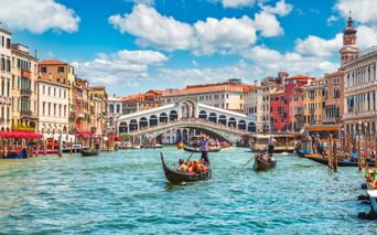 Rialtobrücke über dem Canale Grande in Venedig mit Gondeln und Booten im türkisfarbenen Wasser. Bunte historische Gebäude säumen beide Seiten.