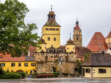 Historisches Ellinger Tor mit gelbem Turm und steinernem Torbogen in Weißenburg. Kirchtürme und traditionelle Gebäude dahinter unter bewölktem Himmel.