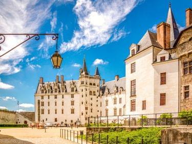 Weißes Château des Ducs de Bretagne mit mehreren Türmen und Spitzen in Nantes, gotische Architektur unter blauem Himmel.