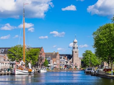 Kanalblick in Lemmer mit traditionellem Segelboot, bunten Häusern und Kirchturm unter blauem Himmel mit weißen Wolken.