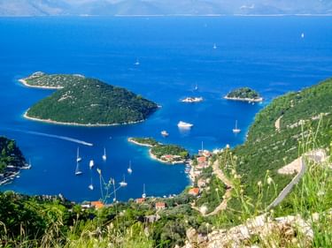 Luftaufnahme der Bucht Okuklje auf der Insel Mljet mit grünen bewaldeten Inseln, Segelbooten im blauen Wasser und einem Küstendorf.