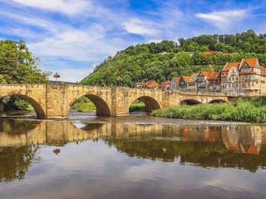 Steinbrücke mit drei Bögen über die Werra in Hann. Münden. Fachwerkhäuser mit orangen Dächern säumen das Flussufer.