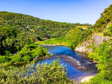 Panoramablick auf den Fluss Eyrieux im grünen Tal der Ardèche mit Radweg rechts und bewaldeten Hügeln im Hintergrund.