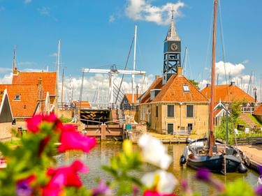 Kanal in Hindeloopen mit traditionellen Booten, Zugbrücke und Kirchturm. Historische Gebäude mit orangefarbenen Dächern säumen das Wasser.