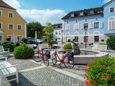 Rote Fahrräder am Brunnen auf dem Marktplatz in Treuchtlingen. Bunte Gebäude und weiße Bänke umgeben den Kopfsteinpflasterplatz.