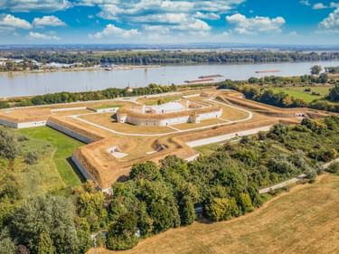 Luftaufnahme einer sternförmigen Festung in Komárom mit weißen Mauern und Erdwällen, umgeben von grünen Feldern und der Donau.