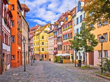 Bunte Fachwerkhäuser säumen die Kopfsteinpflasterstraße in der Weißgerbergasse, Nürnberg. Historische Gebäude in Gelb, Orange und Rosa unter blauem Himmel.