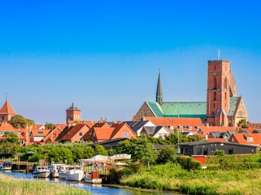 Panoramablick auf Ribe mit roten Ziegeldächern, Kathedrale mit grünem Kupferdach und rotem Turm sowie Booten am Kanal.