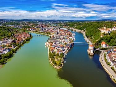 Luftaufnahme von Passau mit historischer Altstadt auf Halbinsel zwischen Flüssen, Brücken verbinden beide Seiten, grüne Wälder umgeben die Stadt.