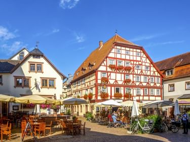 Marktplatz in der Lohrer Altstadt mit traditionellen Fachwerkhäusern, Außengastronomie und Fahrrädern unter blauem Himmel.