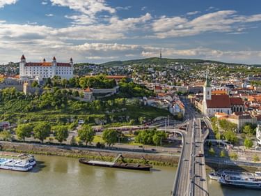 Luftaufnahme von Bratislava mit weißer Burg auf Hügel, Martinsdom, Donau mit Kreuzfahrtschiffen und Brücke zur Altstadt.