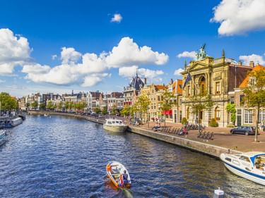 Teylers Museum mit verzierter Fassade an einem Kanal in Haarlem. Historische Gebäude säumen das Ufer mit Booten unter blauem Himmel.